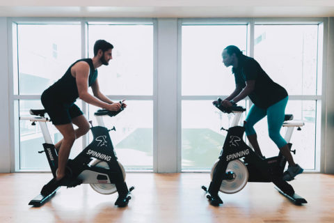 a man and a woman face opposite each other on stationary bikes. There faces are intense and they are pedaling fast.
