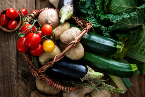 a brown woven basket filled with fresh vegetables such as tomatoes, peppers, zucchini , eggplant and potatoes