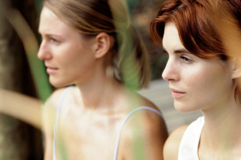 a close up of two women with their hair pulled back wearing light colored workout tank tops. There are intently gazing forward.