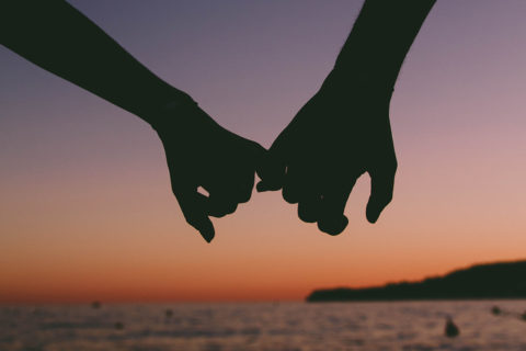 Silhouette of two hangs holding each other by the pinky finger with a pink and purple sunset background
