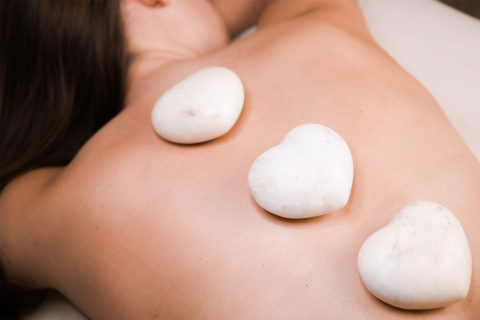a woman lies face down on a massage table. Three white stones balance on her back