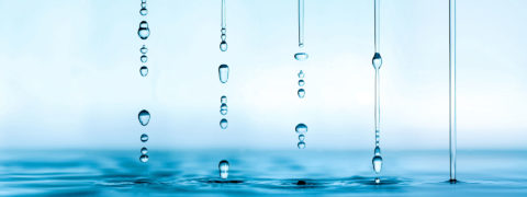 a detail shot of five droplets of water dropping down into a large pool of water