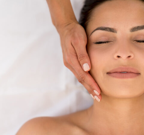 woman receiving a facial with a hand on her face