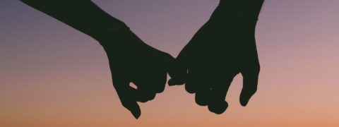 Silhouette of two hangs holding each other by the pinky finger with a pink and purple sunset background