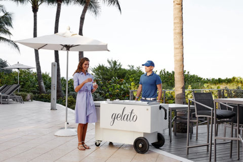 a woman in a chambray dress stops at gelato cart. She smiles as she scoops some onto her spoon.