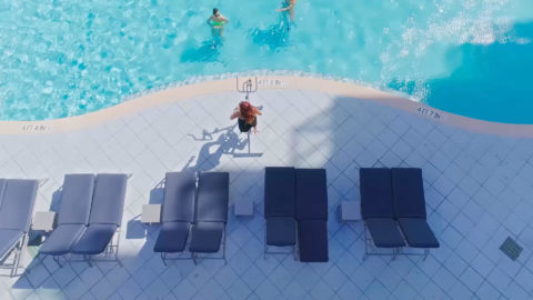 aerial shot of the pool. there is a lifeguard watching two people swim in the pool. There are gray lounge chairs lining the pool