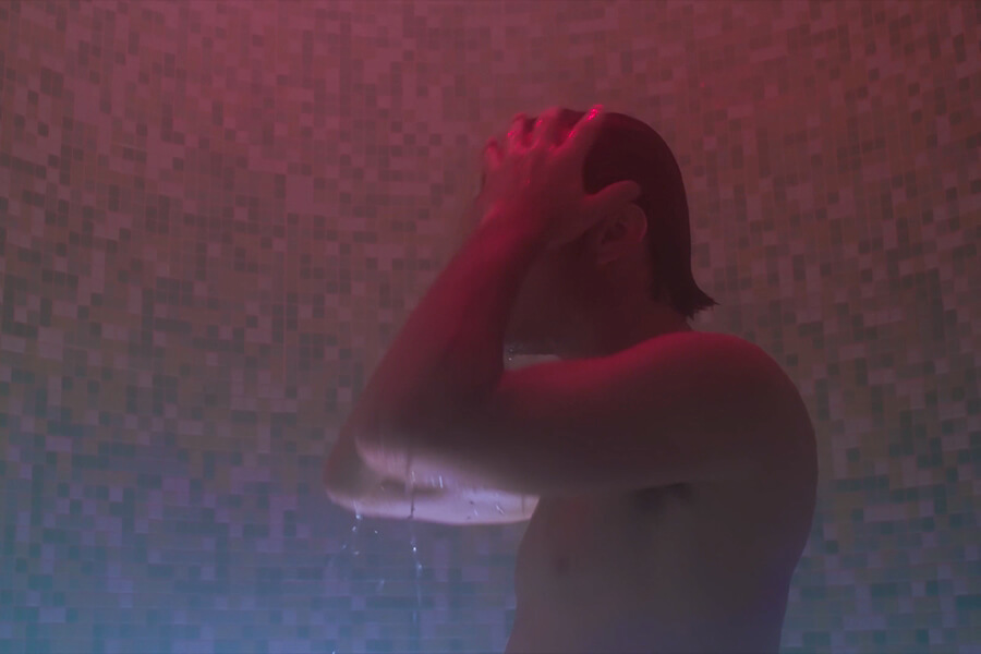 From behind, a hand rests on the back of a head while water falls around shoulders in magenta light at The Spa at Carillon Miami.