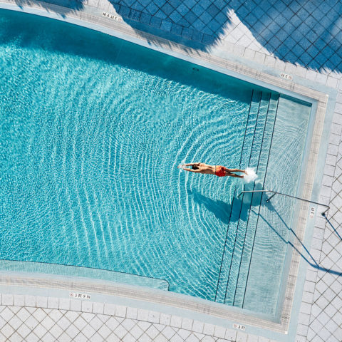 Aerial shot of of a man in red bathing shorts diving into a pool to swim laps/