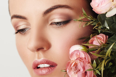 Close up shot of a woman with natural, glowy make-up posing next to pink and green flowers