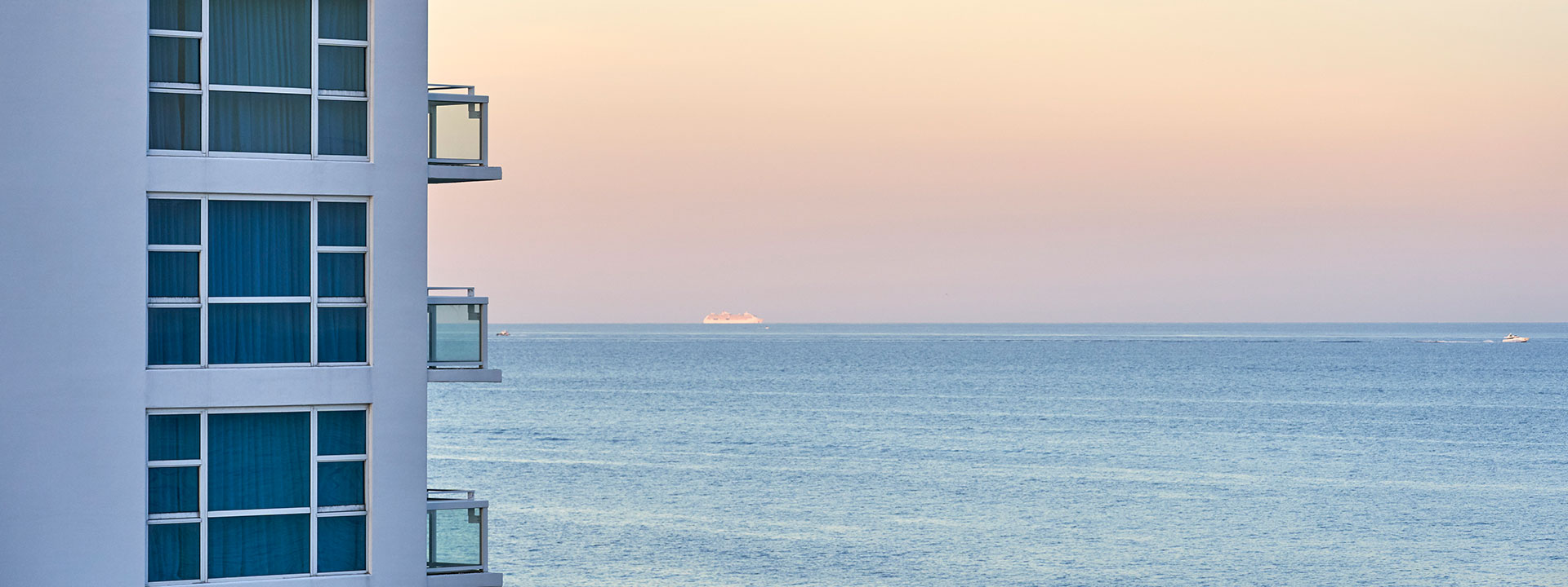 A white building with balconies overlooking the ocean at sunset.