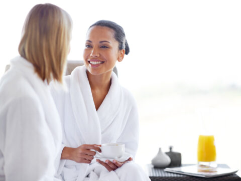 Two young women having coffee in their bathrobes at the day spa
