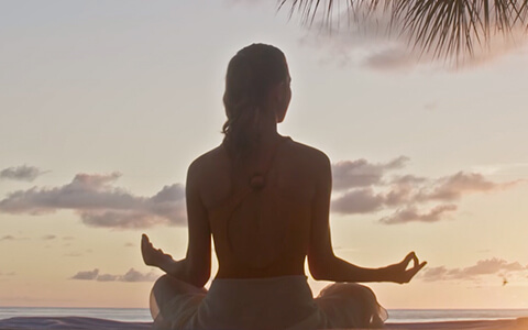 a woman meditating to the sunset