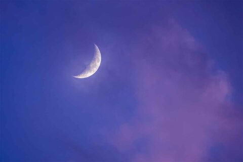 Crescent moon through purple sunset clouds