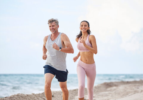 man and woman couple running on the sandy beach with the light blue ocean in the background