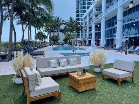 Cushioned wooden furniture and dried plants on top of green turf in pool area
