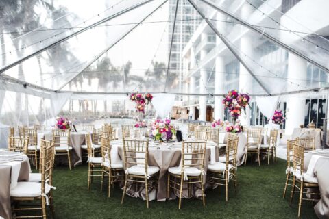 The North Tower Lawn filled with round tables, golden chairs, pink and purple flowers, and a transparent tent hovering over for a wedding celebration