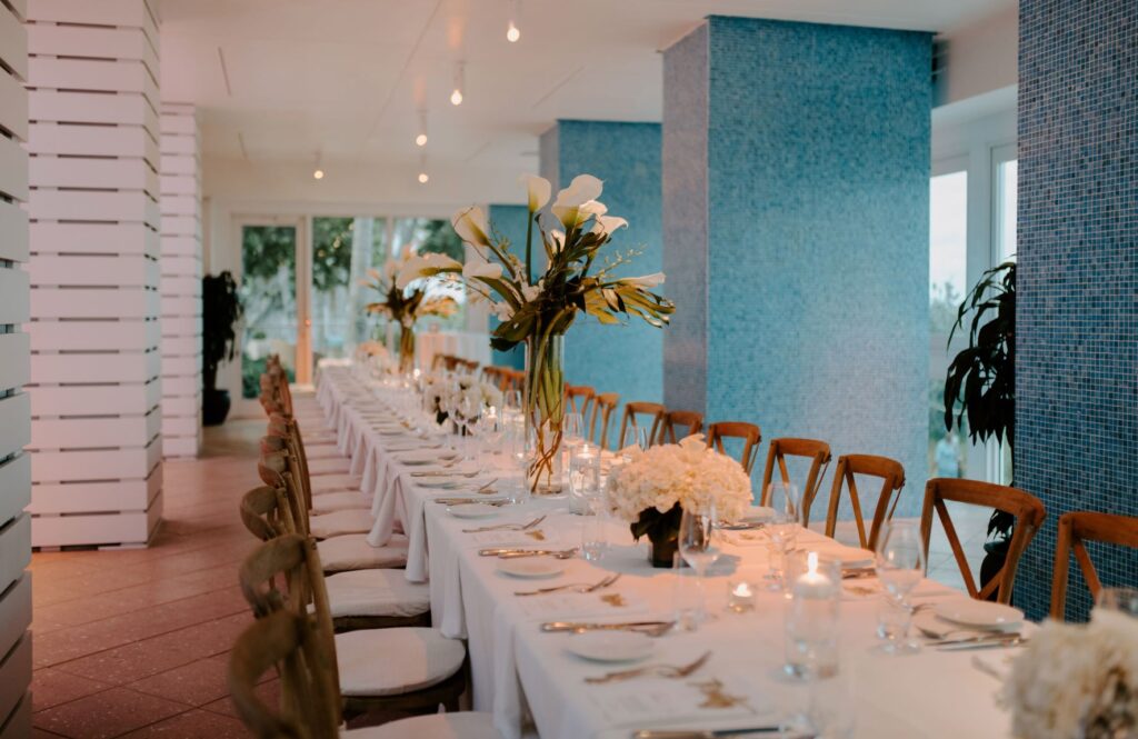 A long, formally set dining table with white tablecloth, flowers, and candles.