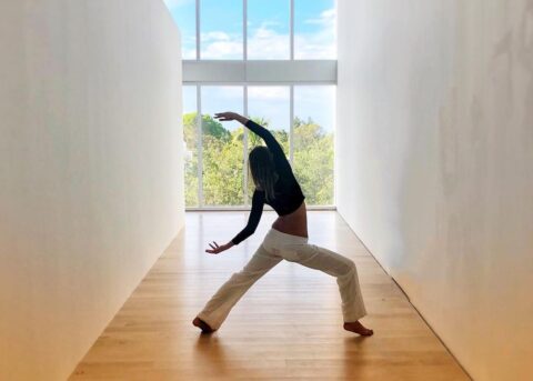 Woman holding warrior 3 position in the center of two white walls