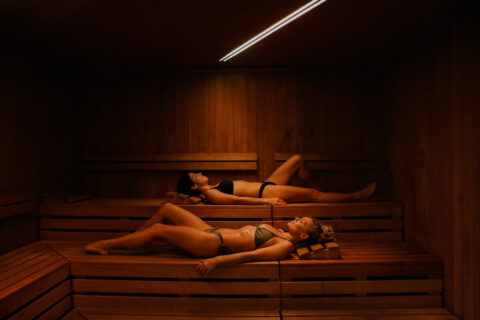 two woman lying in a darkly lit sauna