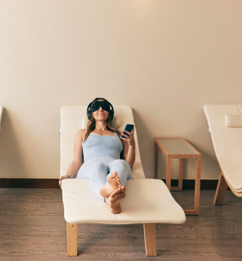 woman laying down white lounger with a head set on in a room